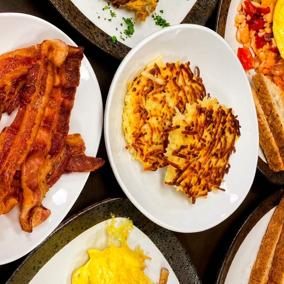 Plates of crispy bacon, golden hash browns, omelets with toast, and a side of beans.