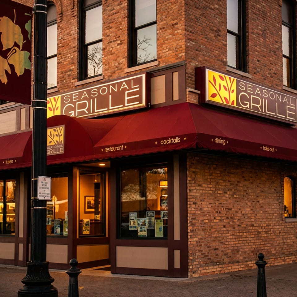 Exterior of Seasonal Grille restaurant with red awnings, brick facade, and glowing windows at dusk.