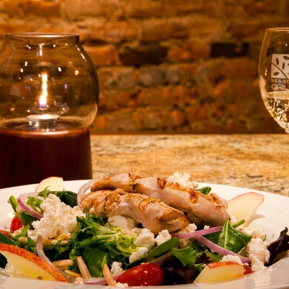 Grilled chicken salad with apples, feta, and red onion, next to a glass of champagne.