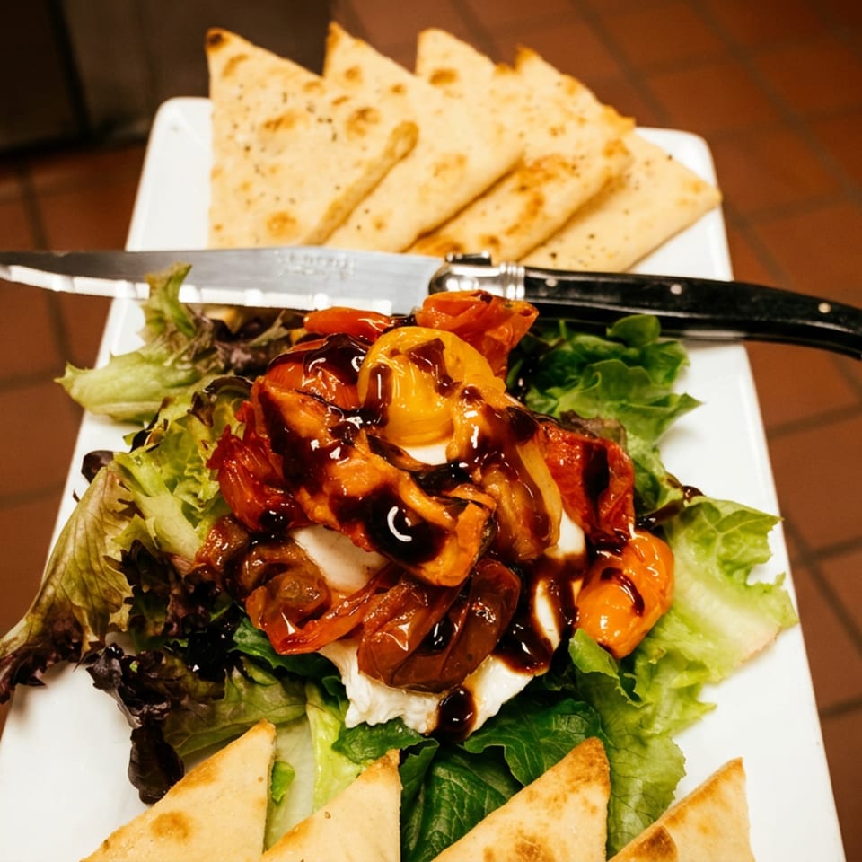Caprese salad with roasted tomatoes, mozzarella, balsamic glaze, and flatbread on a white plate.