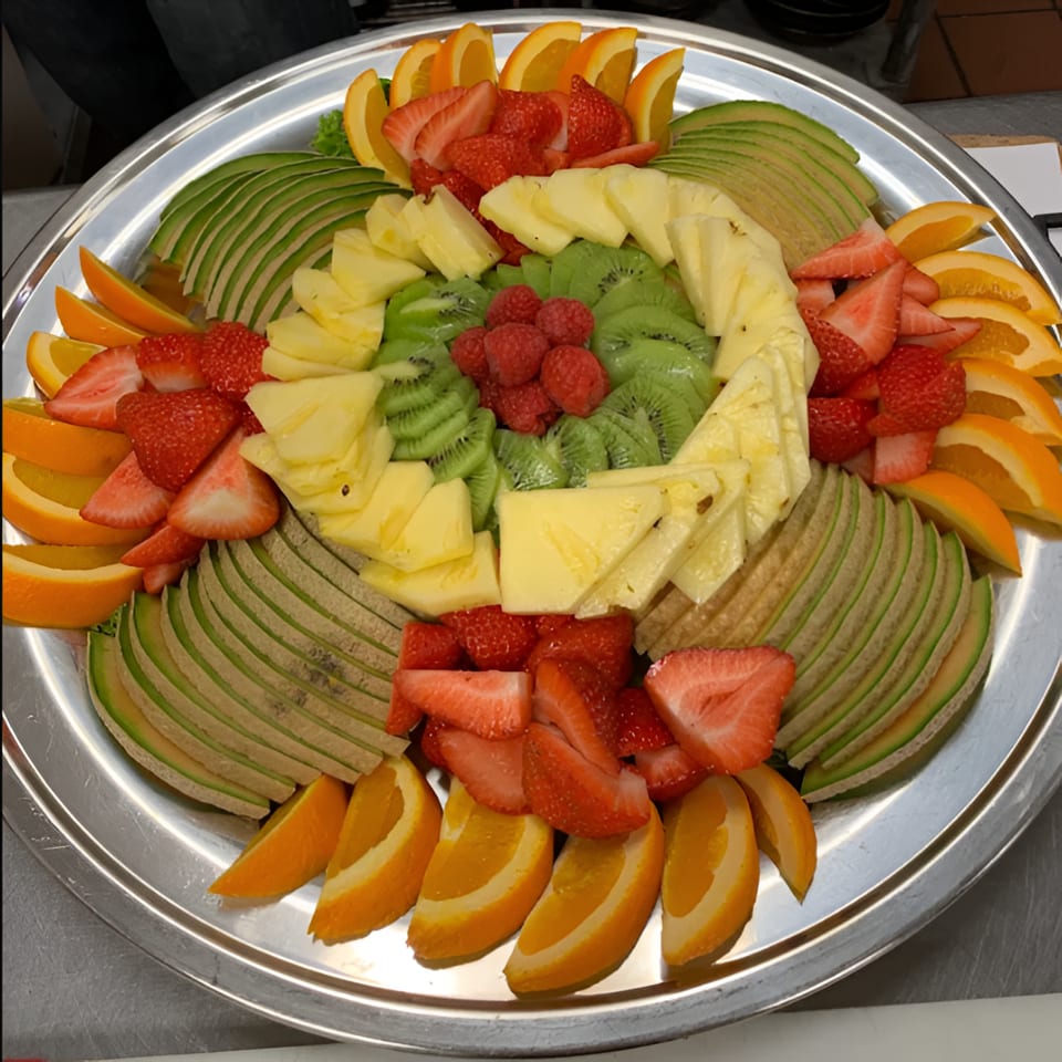 Large platter of sliced oranges, strawberries, pineapple, kiwi, and avocado arranged in colorful concentric patterns.