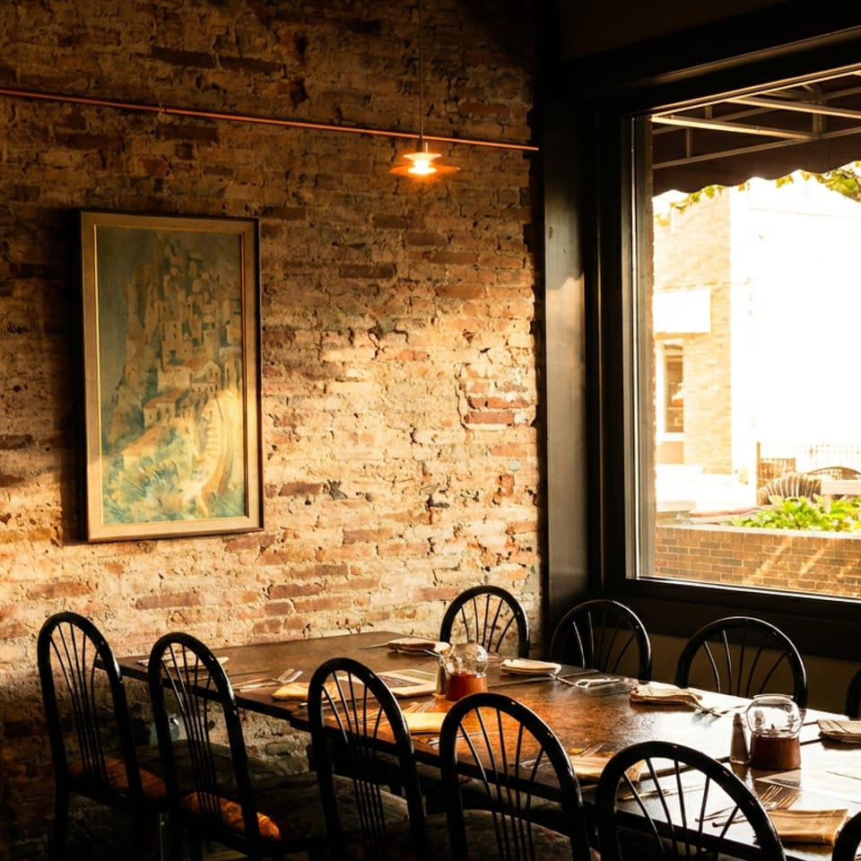 Long dining table set with chairs, next to a brick wall with art and a large window.